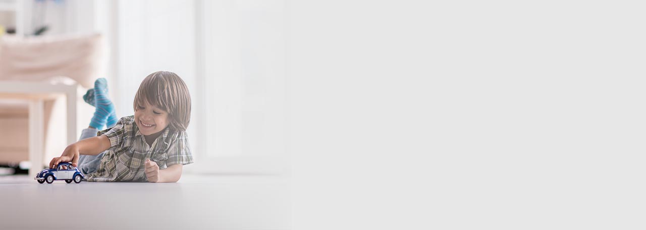 Мальчик играет с игрушечной машинкой на полу.